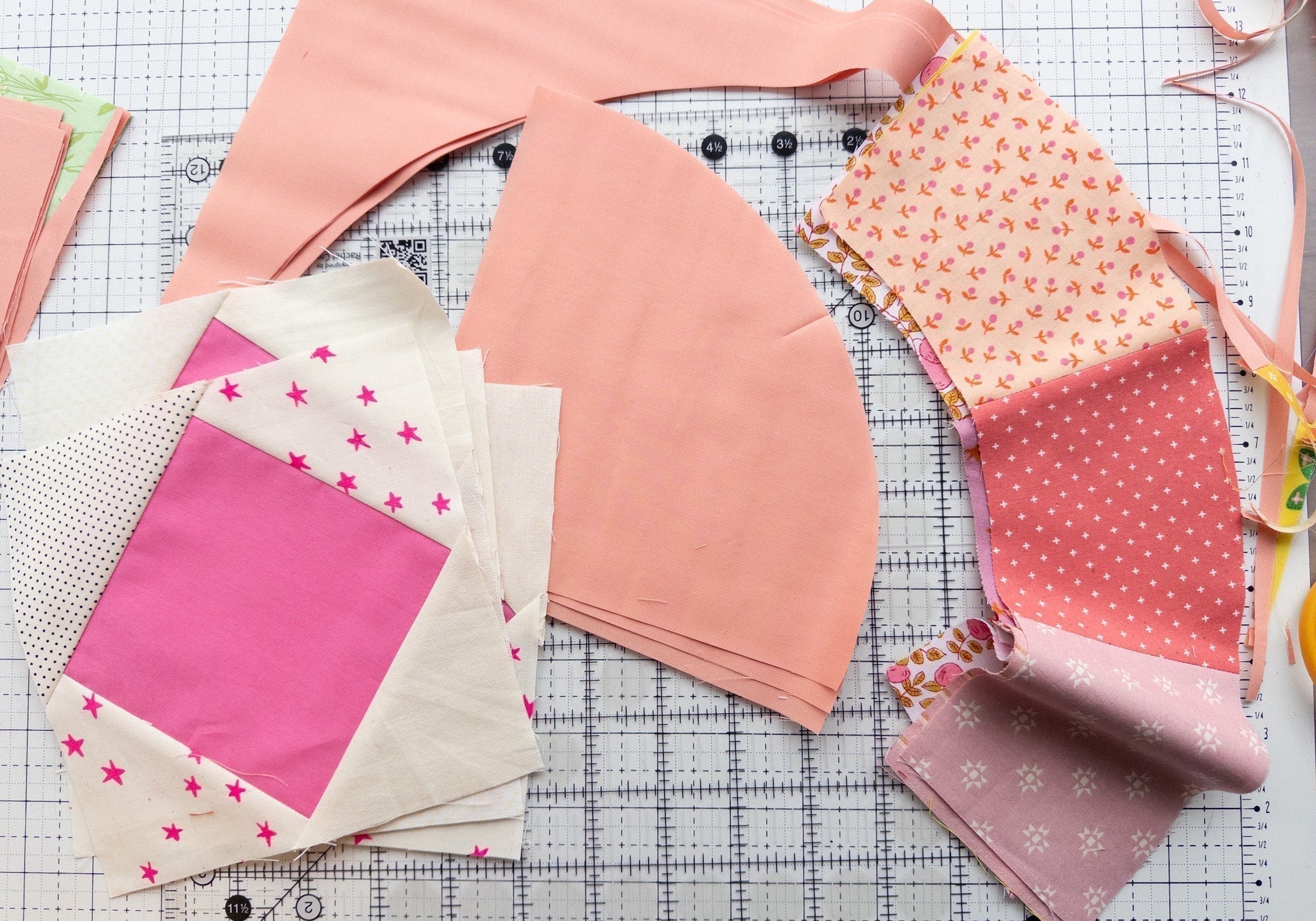Scrappy Moonbeam baby quilt blocks in shades of pink and white next to clear acrylic Moonbeam templates on a gridded cutting mat