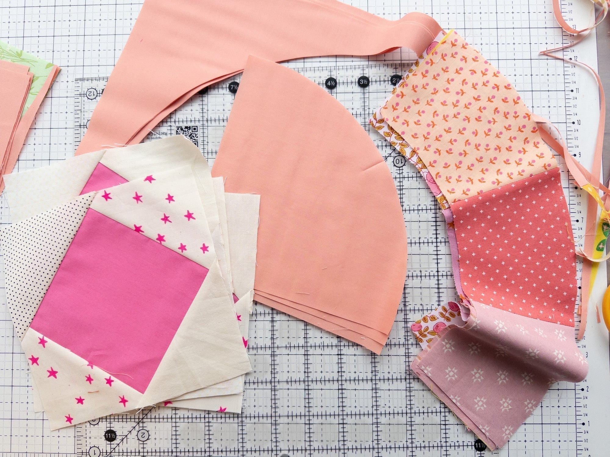Scrappy Moonbeam baby quilt blocks in shades of pink and white next to clear acrylic Moonbeam templates on a gridded cutting mat